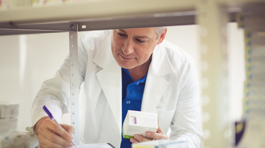 Foto: Eine Person in weißen Kittel überprüft eine Liste im Backoffice einer Apotheke