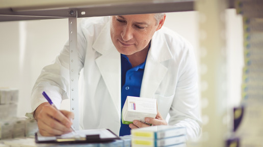 Foto: Eine Person in weißen Kittel überprüft eine Liste im Backoffice einer Apotheke