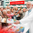 Buchhandlungen verlieren Kalendergeschäft an Apotheken Montage eines Apothekers, der einer Horde Kund:innen Kalender ausgibt.