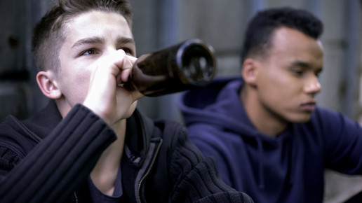 Zwei Jugendliche, einer von ihnen trinkt aus einer Braunglasflasche Bier.
