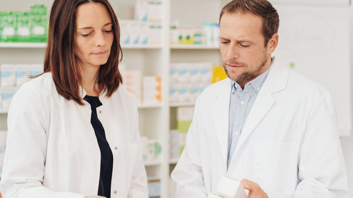 Frau und Mann im Kittel schauen sich in der Apotheke konzentriert etwas an