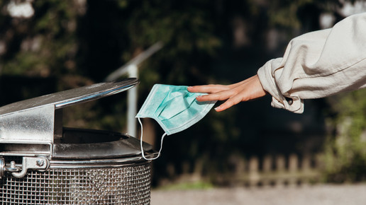 Foto: Eine Person wirft eine Hygienemaske in einen Mülleimer.