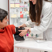 Foto: Eine Person in weißem Kittel legt in der Apotheke einer weiteren Person eine Oberarmmanschette an
