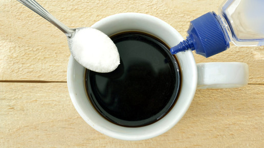 Aufnahme von oben: Eine Tasse Kaffee mit links einem Teelöffel Zucker und rechts Süßstoff aus der Flasche.