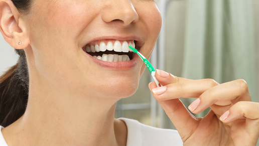 Junge Frau reinigt lächelnd ihre Zahnzwischenräume mit einem SOFT-PICKS® Interdentalreiniger.