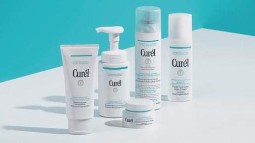  Fünf Curél Hautpflegeprodukte für trockene Haut vor türkis-weißem Hintergrund: Reinigungsschaum & -Gel, Feuchtigkeitscreme & -Fluid, sowie ein Feuchtigkeits-Spray in weißer Verpackung mit türkisfarbenen Akzenten, nebeneinander arrangiert.