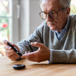 Foto: Eine ältere Person sitzt an einem Tisch und misst ihren Blutzucker