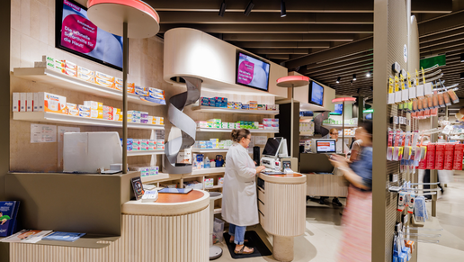 Blick in eine moderne Vor-Ort-Apotheke. Mehrere digitale ApoVid Presenter-Bildschirme zeigen Produktkampagnen über den HV-Tischen, während Mitarbeitende Kundinnen und Kunden bedienen.