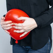Symbolbild für Blähungen, Frau presst einen roten Luftballon an ihren Bauch
