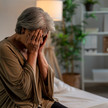 Alte Frau sitzt verzweifelt auf dem Bett
