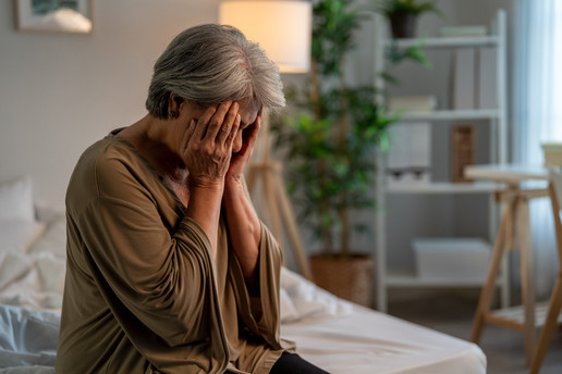 Alte Frau sitzt verzweifelt auf dem Bett