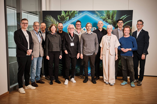 Elf Personen posieren bei einer Veranstaltung vor einer dekorativen Hintergrundwand mit Pflanzenmotiv in einem modernen Innenraum. Quelle: Be.A.Star-Productions 