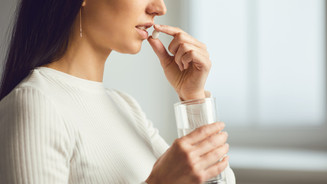 Bundesamt: Kein Lithium zur Nahrungsergänzung Foto: Eine Frau im Profil hält eine Tablette vor ihre Lippen und hält ein Glas Wasser in ihrer Hand.