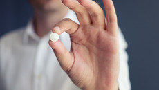 Eine Männerhand hält eine Pille fest.