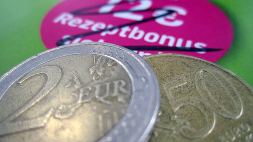 Symbolbild: 12 Euro Rezeptbonus Werbung von DocMorris, durchgestrichen und 2,50 Euro in Münzen dazugelegt