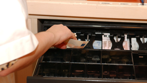 Eine geöffnete Kasse, aus der Geld genommen wird. Mehr dazu im Artikel.