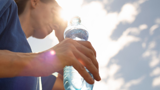 Foto: Eine Frau mit Wasserflasche in der Hand wischt sich den Schweiß von der Stirn.