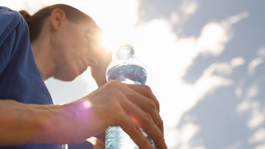 Foto: Eine Frau mit Wasserflasche in der Hand wischt sich den Schweiß von der Stirn.