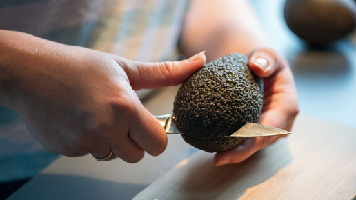 Eine Frau zerteilt eine Avocado in ihren Händen mit einem Messer