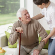 Symbolbild – Pflegerin hilft altem Mann am Stock beim Hinsetzen oder Aufstehen