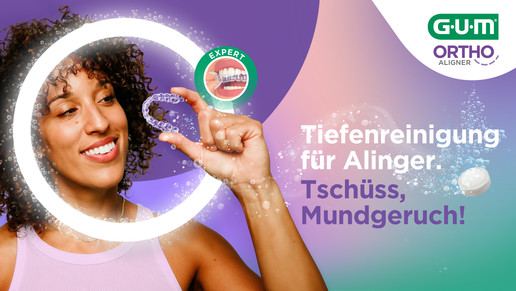 Eine junge Frau hält einen sauberen transparenten Aligner vor sich und freut sich über die effektive Tiefenreinigung dank der neuen GUM® ORTHO ALIGNER Reinigungstabletten, die für Frische, Hygiene und gründliche Reinigung sorgen – ganz nach dem Motto „Hallo Tiefenreinigung, Tschüss Mundgeruch“.