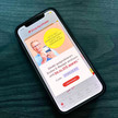 10-Euro-Rabatt: Shop Apotheke erlässt Zuzahlung Foto: Das Bild zeigt ein Smartphone mit geöffneter Shop-Apotheke-App auf einer Tischplatte.
