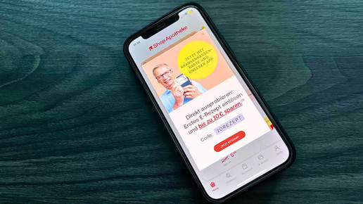 Foto: Das Bild zeigt ein Smartphone mit geöffneter Shop-Apotheke-App auf einer Tischplatte.