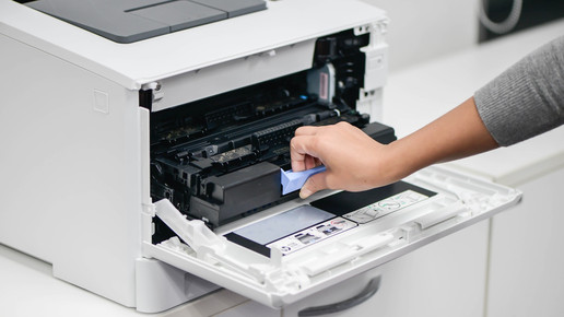 Symbolbild: Eine Frauenhand greift in einen Drucker und zieht dort eine Vorrichtung raus