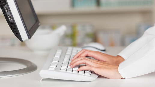 Foto: Eine Person im Kittel tippt in der Apotheke an einem PC.