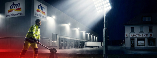 Montage einer Person, die einen Strahler vor einem DM-Logistikzentrum einschaltet.