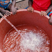 Kinder in Afrika, die um einen großen Behälter sitzen, in den Frischwasser eingelassen wird