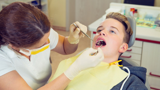 Foto: Eine Zahnärztin untersucht einen Jugendlichen in der Zahnarztpraxis