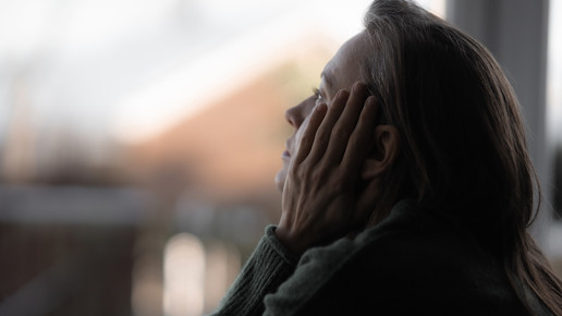 Foto: Eine Frau mittleren Alters schaut nachdenklich aus dem Fenster.