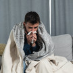 Respiratorische Erkrankungen auf dem Höchststand Symbolbild: Mann sitzt in Decke gewickelt auf einer Couch und putzt sich die Nase