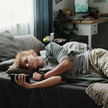 Foto: Eine jugendliche Person liegt auf ihrem Bett und schaut auf ihr Smartphone