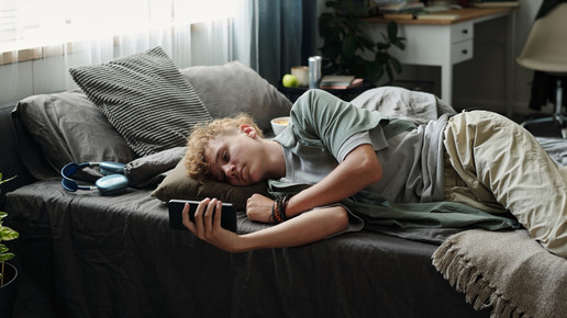 Foto: Eine jugendliche Person liegt auf ihrem Bett und schaut auf ihr Smartphone