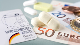 Foto: Tabletten, Geldscheine und Münzen neben einer Versichertenkarte auf einer Oberfläche.