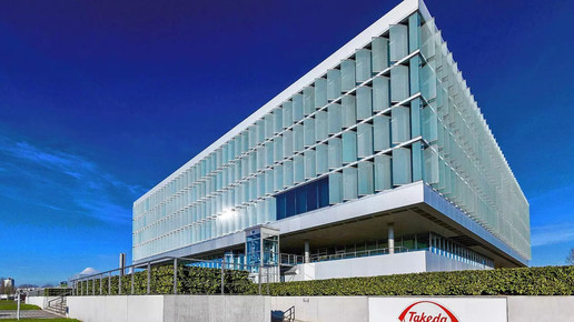 Bisherige Deutschlandzentrale von Takeda, modernes Glasgebäude vor blauem Himmel