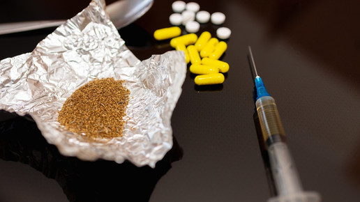 Bild mit braunen Pulver in Alufolie, gelben Kapseln, weißen Tabletten einen Teil eines Löffels und eine mit brauner Flüssigkeit gefüllten Spritze.