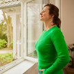 Eine Frau steht am Fenster und atmet befreit durch.