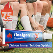 Fussballmanschaft sitzt auf einer Bank auf dem Rasen. Nur die Stollen sind sichtbar und ein übergroßes Packshot der Finalgon Tube und das 75 Jahre Jubiläumslogo. Finalgon- Schon immer Teil des Spiels