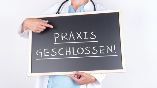 Symbolbild: Person im kittel hät Schild mit der Aufschrift „Praxis geschlossen“