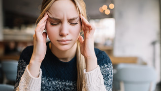 Symbolbild: Junge Frau hält sich mit geschlossenen Augen die Finger an die Schläfen
