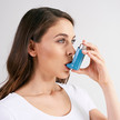 Junge Frau verwendet einen Dosier- bzw. Pumpinhalator während einer Asthmaattacke und atmet das Medikament ein.