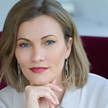 Porträtbild von Ira Kröswang. Eine Frau mit schulterlangem, blonden Haar, die selbstbewusst in die Kamera blickt.