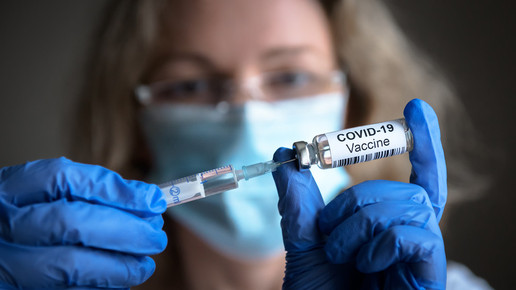 Frau mit blauen Handschuhen hält Corona-Impfstoff in der Hand