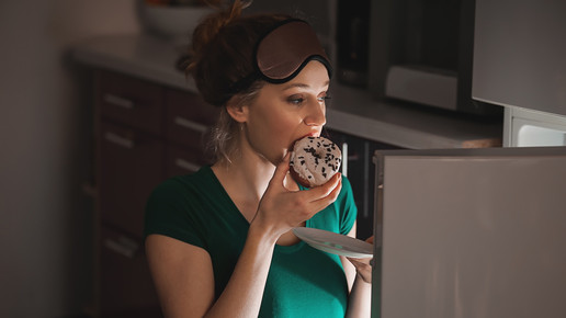Foto: Eine Person mit Schlafmaske auf der Stirn ist einen Donut im Dunkeln