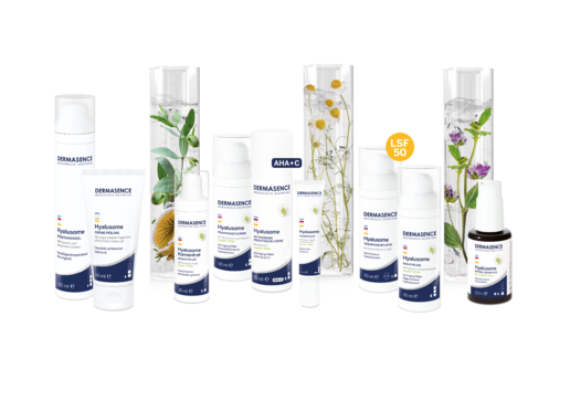 DERMASENCE Hyalusome Pflegeserie mit mehreren weißen Hautpflegeprodukten in unterschiedlichen Größen, angeordnet vor dekorativen Glaszylindern mit Pflanzen; sichtbar markiert sind AHA, Vitamin C und LSF 50.
