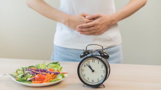 Foto: Eine Person hinter vor einem Salat und einem Wecker, die Arme vor dem Bauch verschränkt