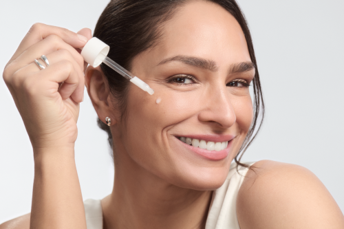 Nahaufnahme einer Frau mit Pipette und Serumtröpfchen auf der Wange. Sie lächelt und vermittelt das Gefühl gepflegter, glatter Haut – passend zur Anti-Aging-Wirkung des Eucerin Serums.